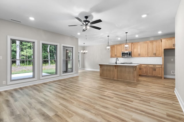 kitchen featuring decorative backsplash, a kitchen island with sink, hanging light fixtures, and light wood-type flooring