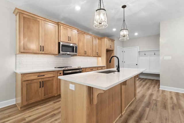 kitchen featuring sink, hanging light fixtures, appliances with stainless steel finishes, a kitchen island with sink, and backsplash