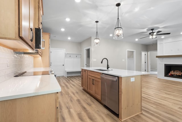 kitchen with appliances with stainless steel finishes, pendant lighting, an island with sink, sink, and light hardwood / wood-style flooring