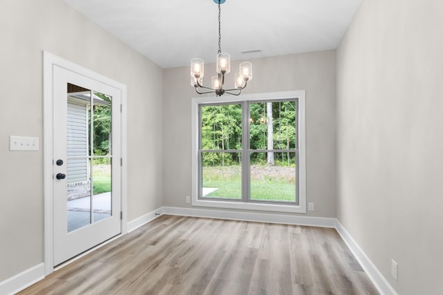 unfurnished dining area with an inviting chandelier and light hardwood / wood-style flooring