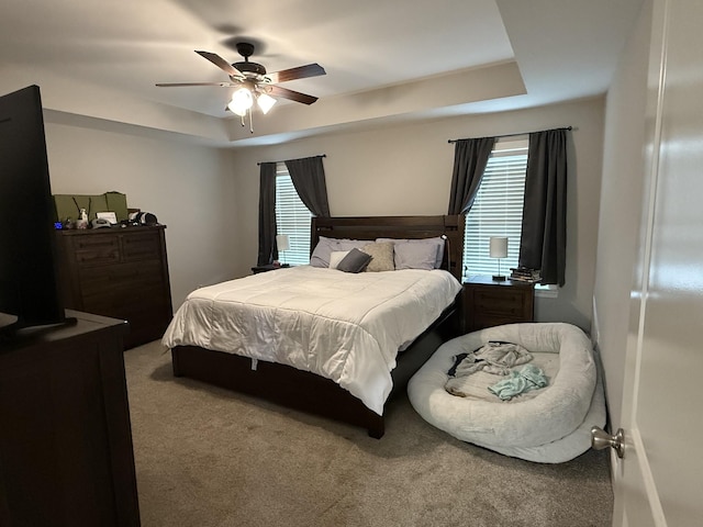 carpeted bedroom featuring ceiling fan and a tray ceiling