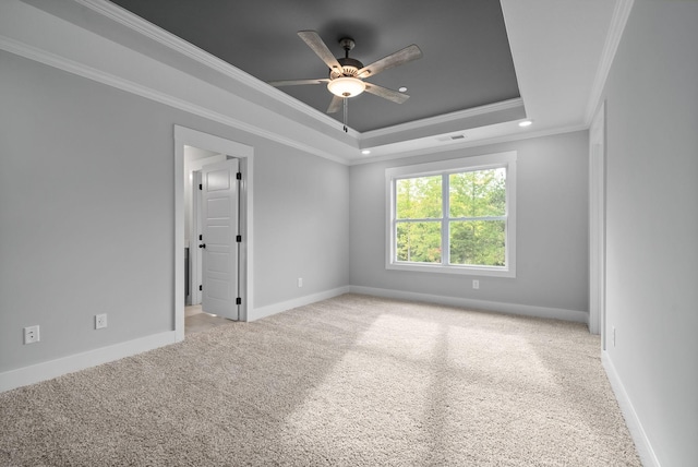 spare room with a tray ceiling, ornamental molding, light colored carpet, and ceiling fan