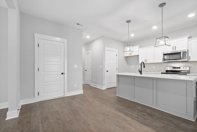 kitchen with white cabinetry, hanging light fixtures, appliances with stainless steel finishes, dark hardwood / wood-style flooring, and an island with sink