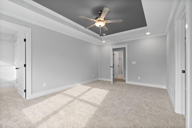 unfurnished bedroom featuring crown molding, ceiling fan, a tray ceiling, light carpet, and a spacious closet