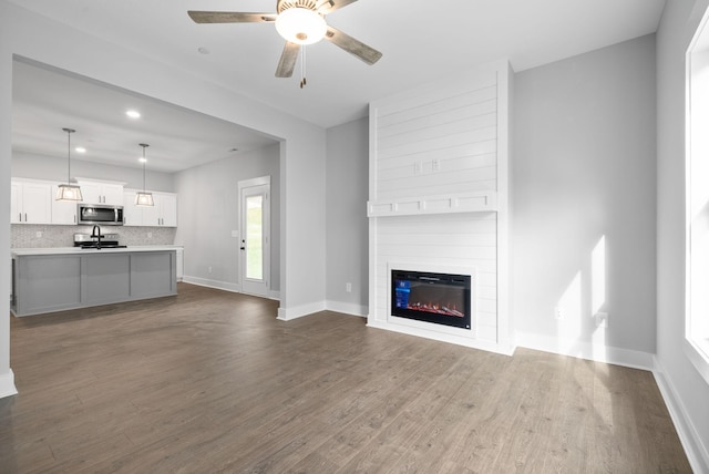 unfurnished living room with sink, a large fireplace, hardwood / wood-style flooring, ceiling fan, and plenty of natural light