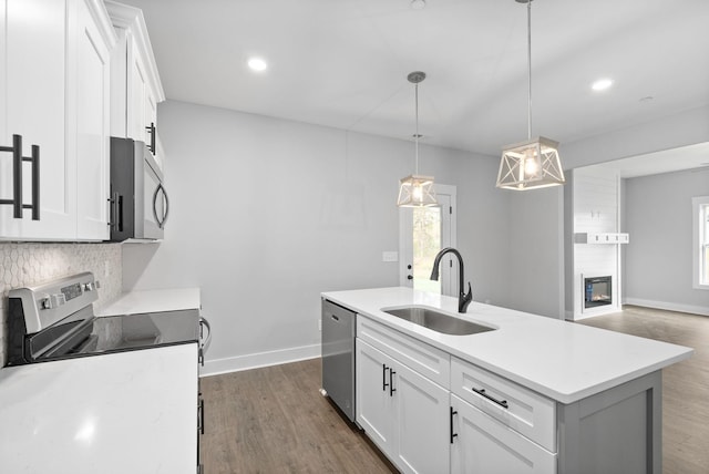 kitchen featuring sink, decorative light fixtures, a center island with sink, stainless steel appliances, and white cabinets