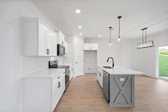 kitchen featuring decorative light fixtures, white cabinetry, sink, a kitchen island with sink, and stainless steel appliances