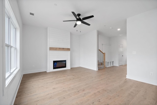 unfurnished living room featuring ceiling fan, a healthy amount of sunlight, a fireplace, and light hardwood / wood-style floors