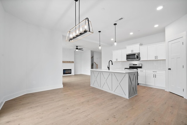 kitchen with white cabinetry, tasteful backsplash, decorative light fixtures, appliances with stainless steel finishes, and a kitchen island with sink