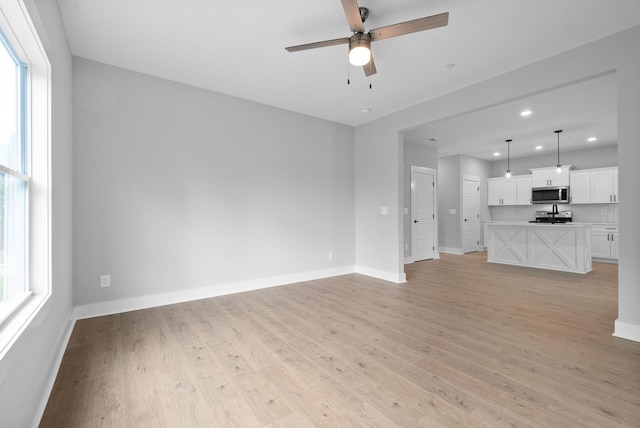 unfurnished living room with a wealth of natural light, ceiling fan, and light hardwood / wood-style flooring