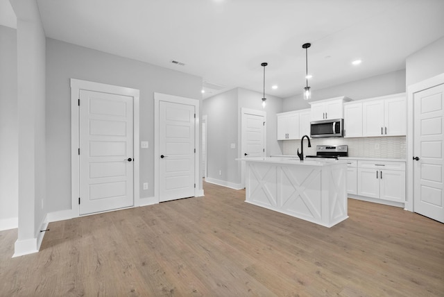 kitchen with white cabinetry, a center island with sink, appliances with stainless steel finishes, pendant lighting, and decorative backsplash