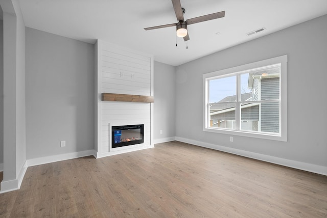 unfurnished living room with ceiling fan, a large fireplace, and light wood-type flooring