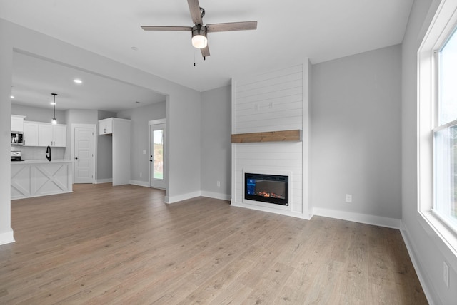 unfurnished living room with light hardwood / wood-style floors, a large fireplace, and ceiling fan