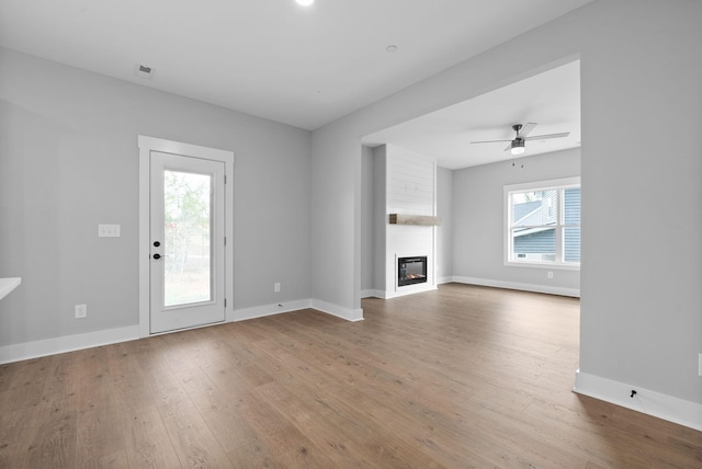 unfurnished living room with ceiling fan, a large fireplace, and light wood-type flooring