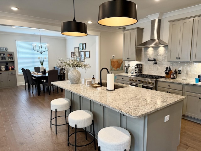 kitchen with an island with sink, high end stove, sink, and wall chimney exhaust hood