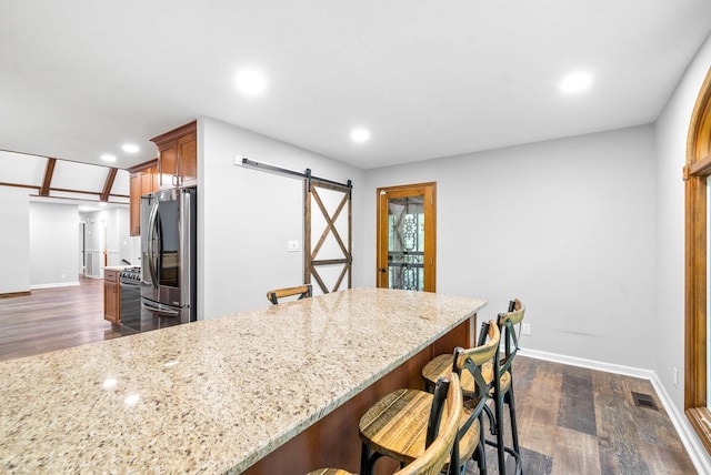 kitchen featuring stainless steel fridge, light stone countertops, a barn door, and a breakfast bar