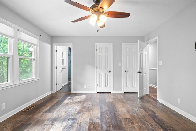 unfurnished bedroom with ensuite bathroom, dark hardwood / wood-style floors, two closets, and ceiling fan