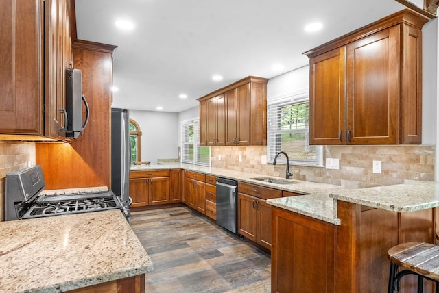 kitchen featuring appliances with stainless steel finishes, a breakfast bar, sink, kitchen peninsula, and light stone countertops