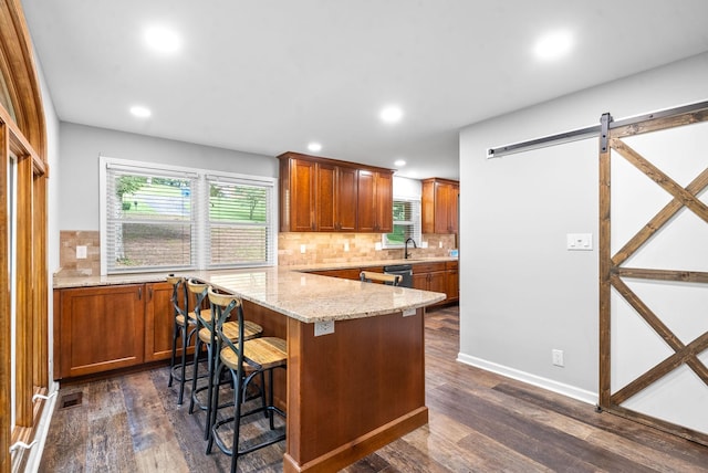 kitchen featuring a breakfast bar, a center island, light stone countertops, dark hardwood / wood-style flooring, and a barn door