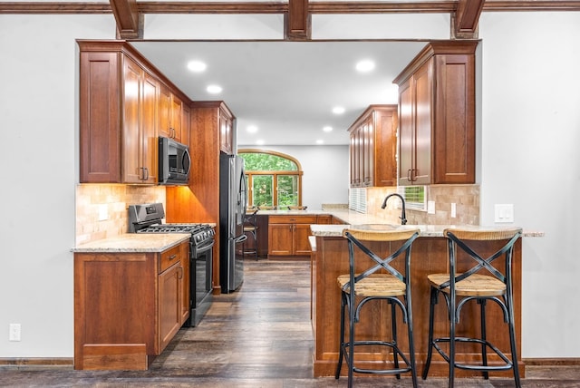 kitchen with sink, dark wood-type flooring, appliances with stainless steel finishes, light stone countertops, and kitchen peninsula