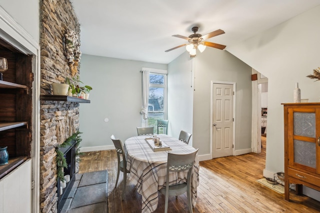 dining area featuring a stone fireplace, light hardwood / wood-style flooring, ceiling fan, and vaulted ceiling