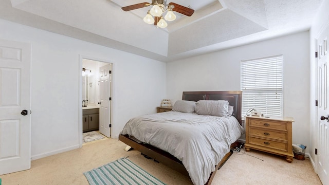 bedroom featuring a tray ceiling, baseboards, light colored carpet, and ensuite bath