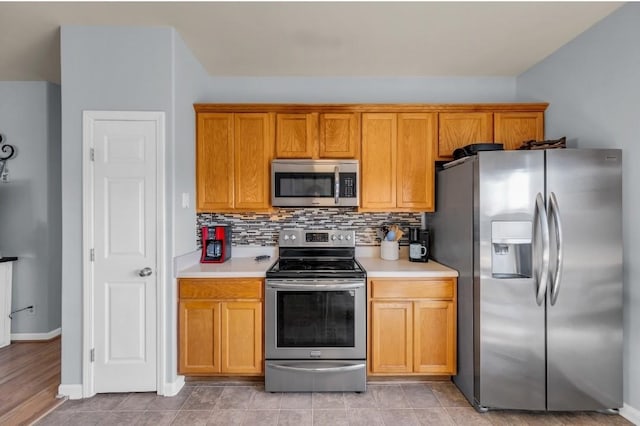 kitchen featuring brown cabinetry, backsplash, appliances with stainless steel finishes, and light countertops