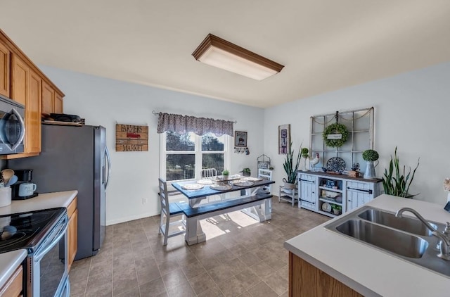 kitchen with brown cabinetry, baseboards, stainless steel appliances, a sink, and light countertops