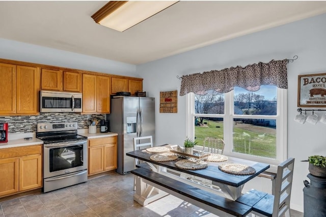 kitchen featuring light countertops, backsplash, brown cabinetry, and appliances with stainless steel finishes