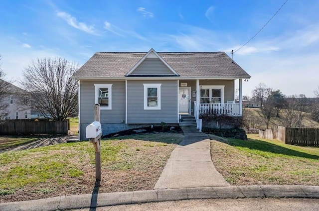 bungalow-style house with roof with shingles, covered porch, a front lawn, and fence