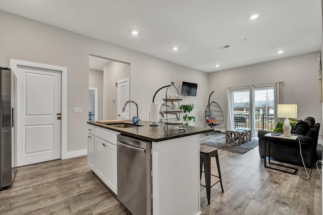 kitchen with sink, white cabinetry, light wood-type flooring, appliances with stainless steel finishes, and an island with sink