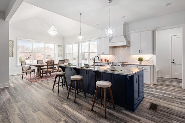 kitchen featuring premium range hood, white cabinetry, hanging light fixtures, and a center island with sink