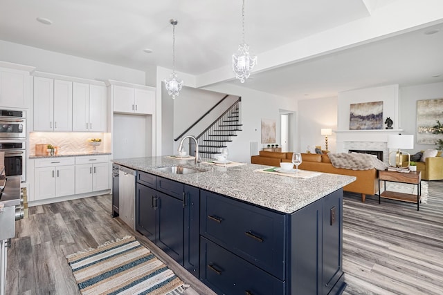 kitchen featuring decorative light fixtures, white cabinetry, sink, a kitchen island with sink, and light wood-type flooring