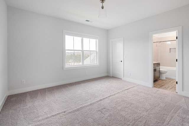 unfurnished bedroom featuring light colored carpet and ensuite bath