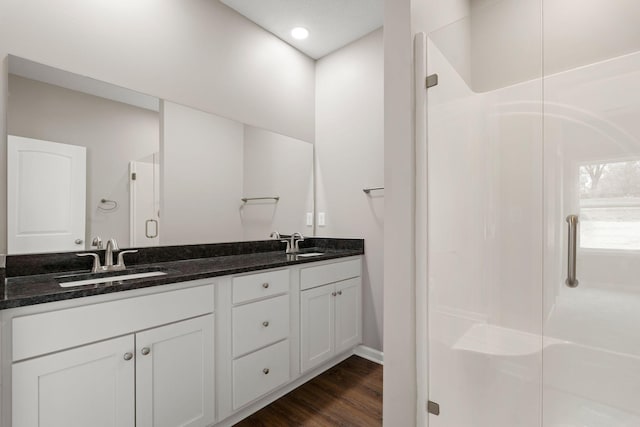 full bath with double vanity, a sink, a shower stall, and wood finished floors
