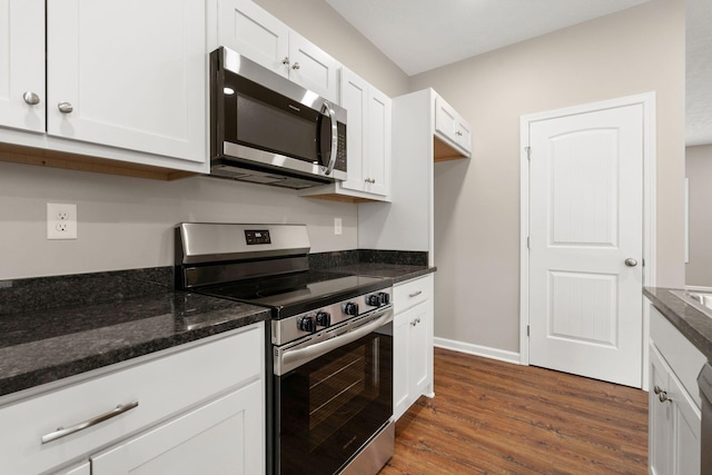 kitchen with dark wood-style flooring, white cabinets, baseboards, stainless steel appliances, and dark stone counters