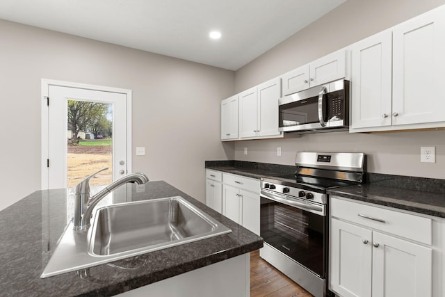 kitchen with a sink, white cabinets, wood finished floors, and appliances with stainless steel finishes