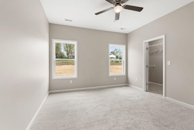 unfurnished bedroom with a walk in closet, carpet flooring, baseboards, ceiling fan, and visible vents
