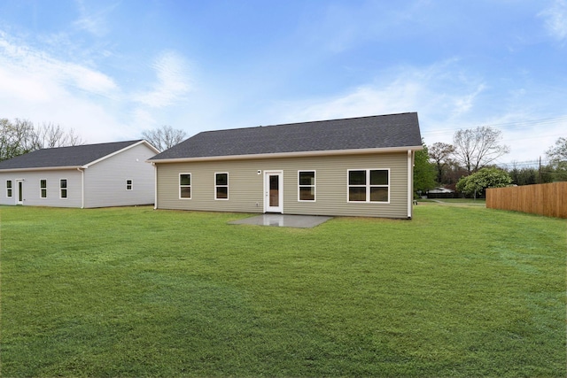 rear view of house featuring fence, a shingled roof, a patio area, and a lawn