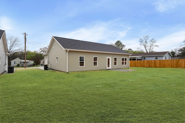 back of property featuring a shingled roof, central air condition unit, fence, and a yard