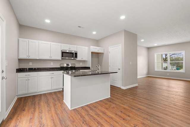 kitchen featuring open floor plan, stainless steel appliances, baseboards, an island with sink, and wood finished floors