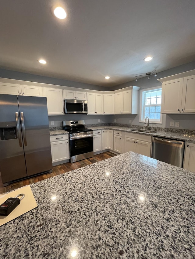 kitchen with white cabinetry, stainless steel appliances, sink, and stone counters