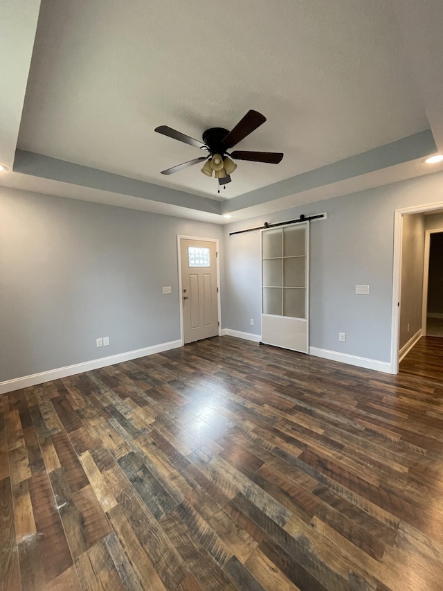 empty room featuring ceiling fan, a barn door, dark hardwood / wood-style flooring, and a tray ceiling