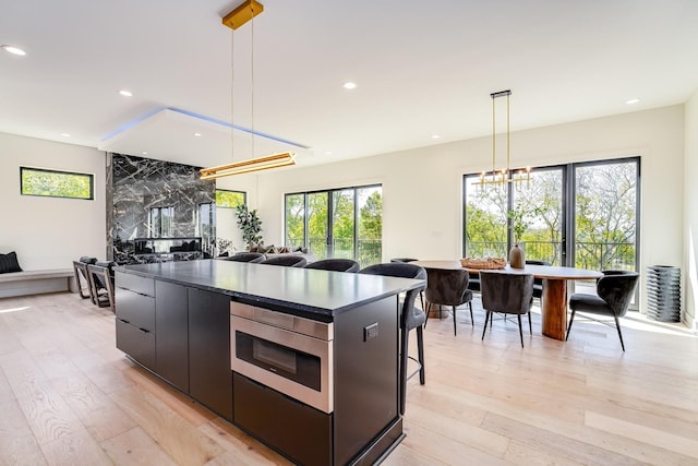 kitchen featuring hanging light fixtures, a kitchen bar, light hardwood / wood-style flooring, and stainless steel microwave