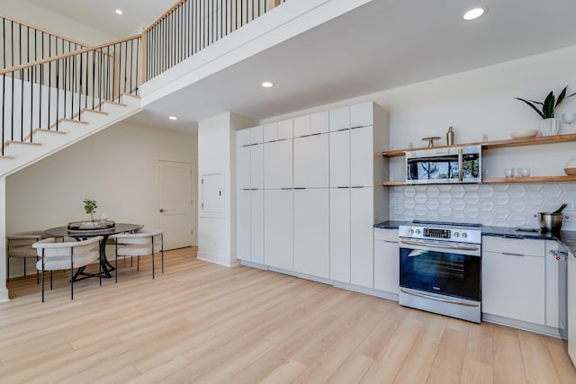 kitchen featuring light wood-type flooring, appliances with stainless steel finishes, white cabinets, a high ceiling, and backsplash