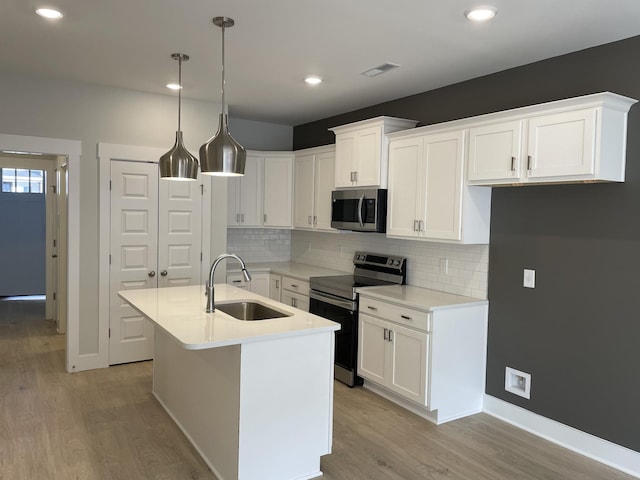 kitchen with decorative light fixtures, sink, white cabinets, a kitchen island with sink, and stainless steel appliances