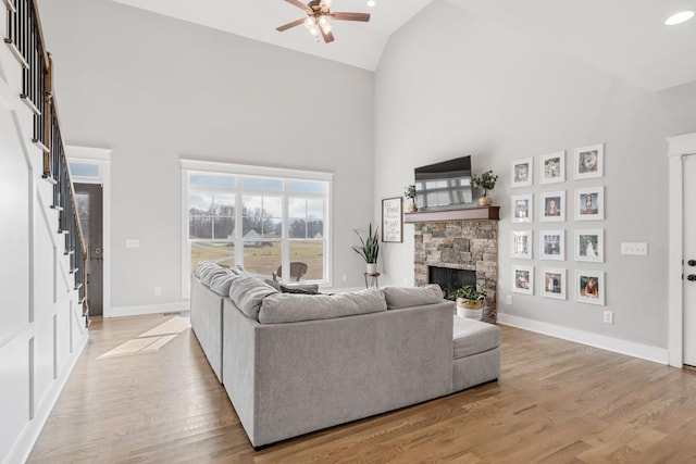 living room featuring ceiling fan, a stone fireplace, high vaulted ceiling, and light hardwood / wood-style floors