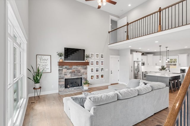 living room featuring ceiling fan, a towering ceiling, a fireplace, and light hardwood / wood-style floors