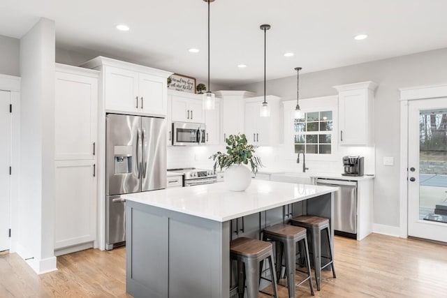 kitchen featuring white cabinetry, hanging light fixtures, light hardwood / wood-style flooring, a kitchen island, and stainless steel appliances