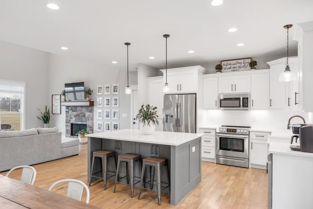 kitchen featuring white cabinetry, stainless steel appliances, decorative light fixtures, and a center island